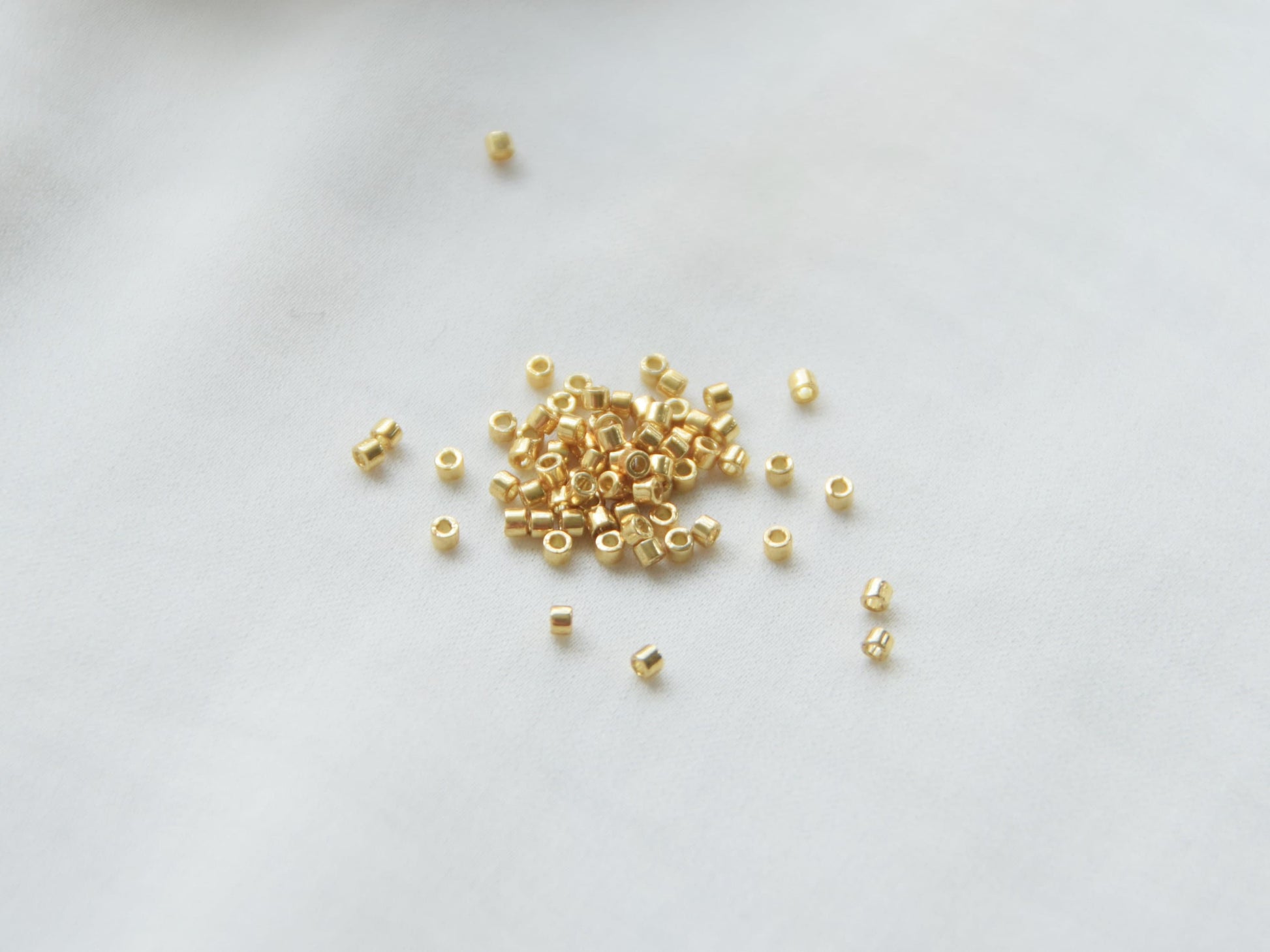 A few beads spread on a white background. The beads are gold colored, 1.6mm in size and cylindrical in shape.