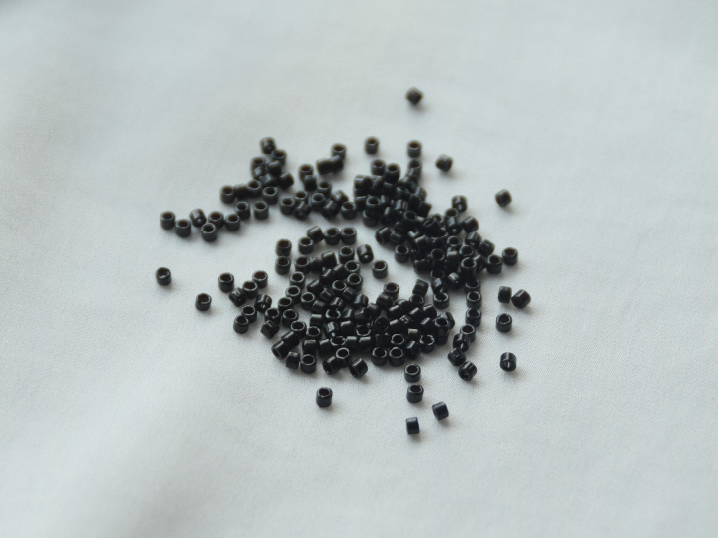 A few beads spread on a white background. The beads are opaque, 1.6mm in size and cylindrical in shape.
Miyuki Delica beads, opaque black.