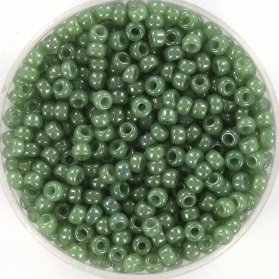 Translucent green seed beads, 3mm in size and round in shape. The image shows a round bowl full of seed beads on a white background