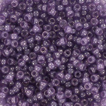 Translucent purple seed beads, 2mm in size and round in shape. The image is a close-up of a bowl of full of seed beads so that the beads fill the entire image