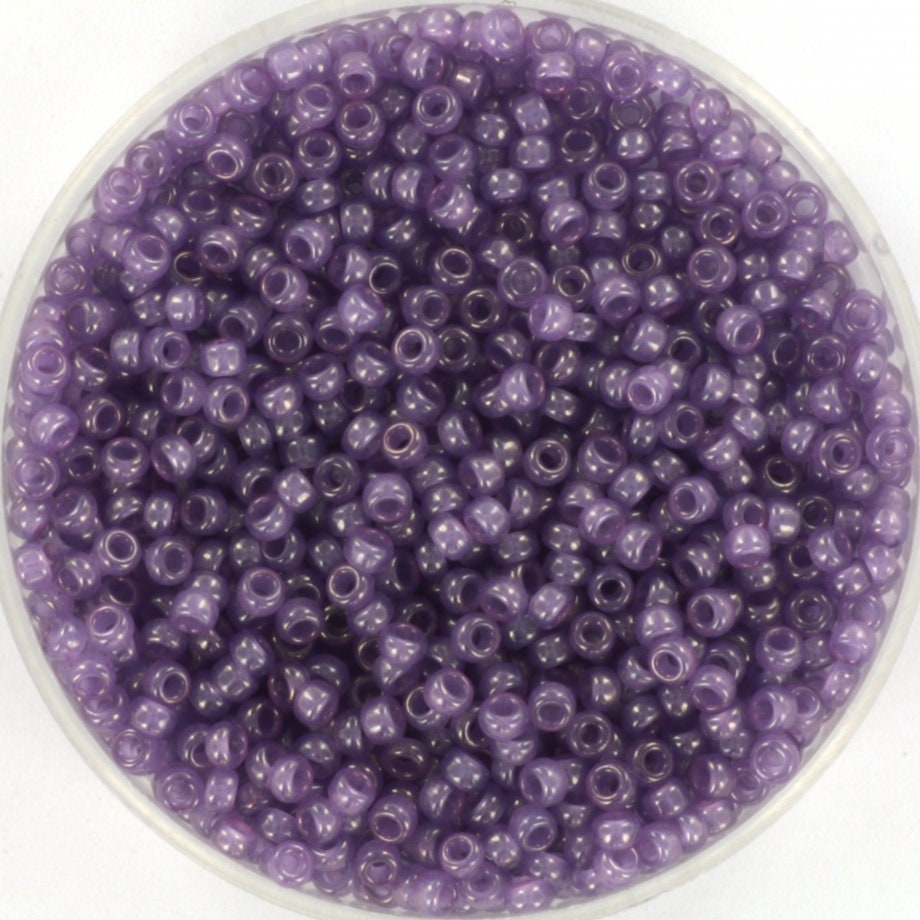 Translucent purple seed beads, 2mm in size and round in shape. The image shows a round bowl full of seed beads on a white background