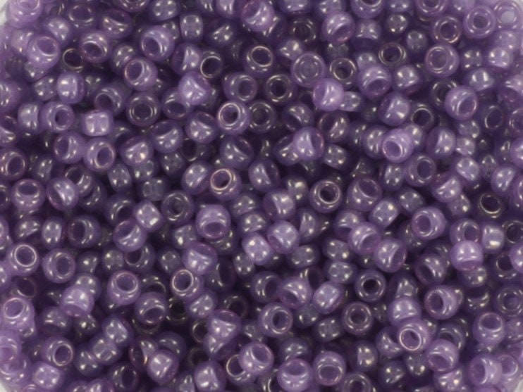 Translucent purple seed beads, 2mm in size and round in shape. The image is a close-up of a bowl of full of seed beads so that the beads fill the entire image