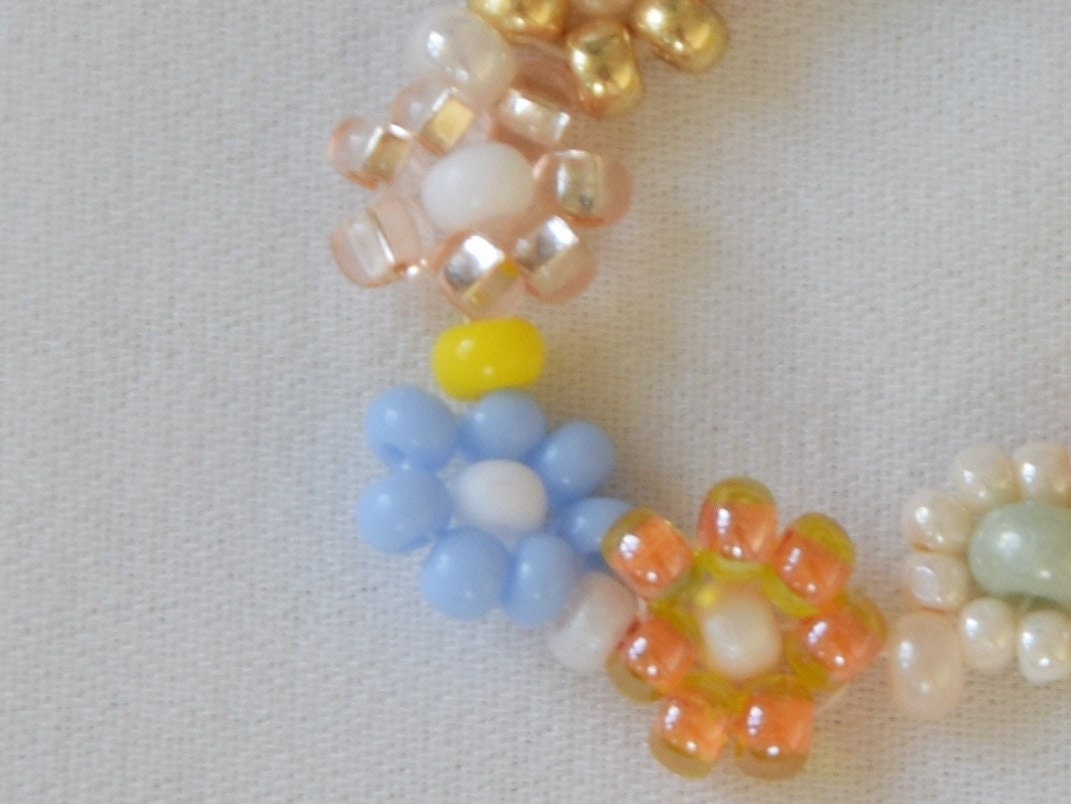 Close-up of one half of the ring with a transparent light pink flower, a light blue one, a transparent orange one and a cream colored flower. The ring lays flat on a white surface.