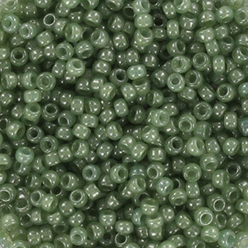 Translucent green seed beads, 2mm in size and round in shape. The image is a close-up of a bowl of full of seed beads so that the beads fill the entire image