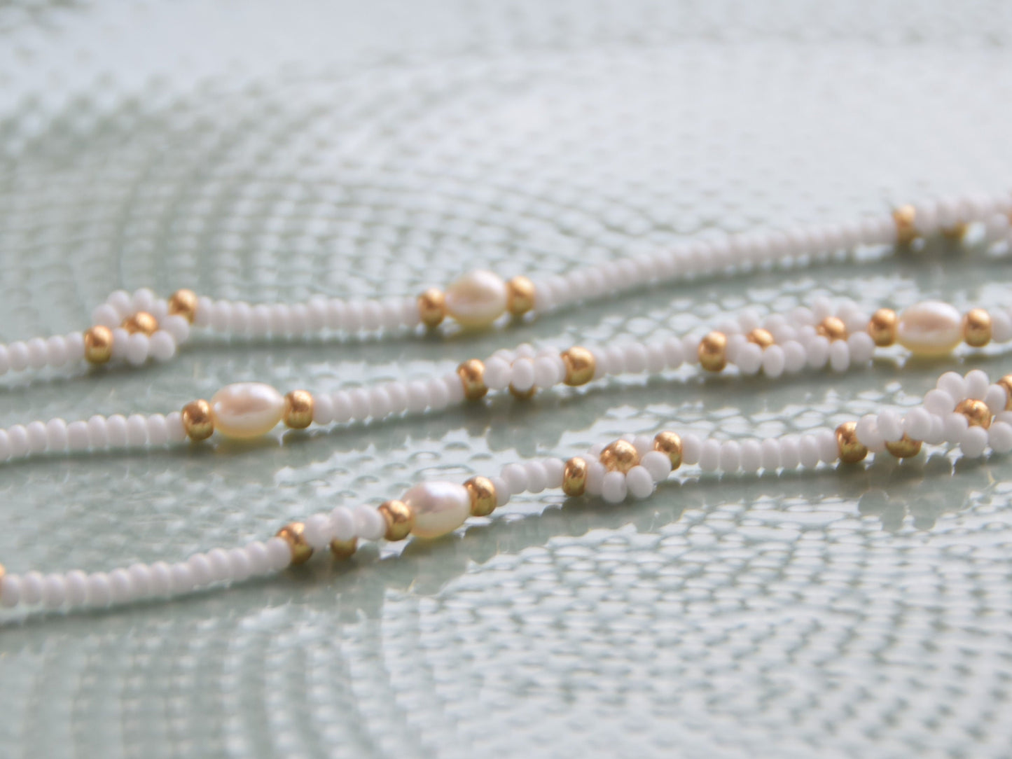 Three strands of necklaces. The necklaces are made with white and gold seed beads and freshwater pearls.