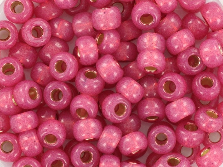 Pink seed beads silverlined, 4mm in size and round in shape. The image is a close-up of a bowl of full of seed beads so that the beads fill the entire image