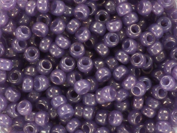 Translucent purple seed beads, 3mm in size and round in shape. The image is a close-up of a bowl of full of seed beads so that the beads fill the entire image