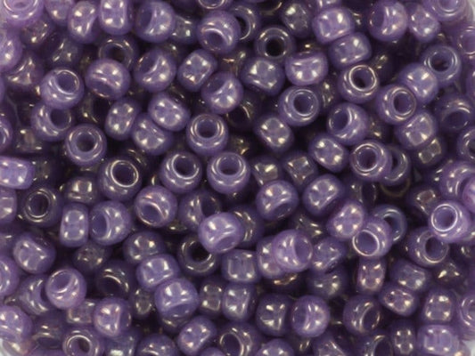 Translucent purple seed beads, 3mm in size and round in shape. The image is a close-up of a bowl of full of seed beads so that the beads fill the entire image