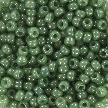 Translucent green seed beads, 3mm in size and round in shape. The image is a close-up of a bowl of full of seed beads so that the beads fill the entire image