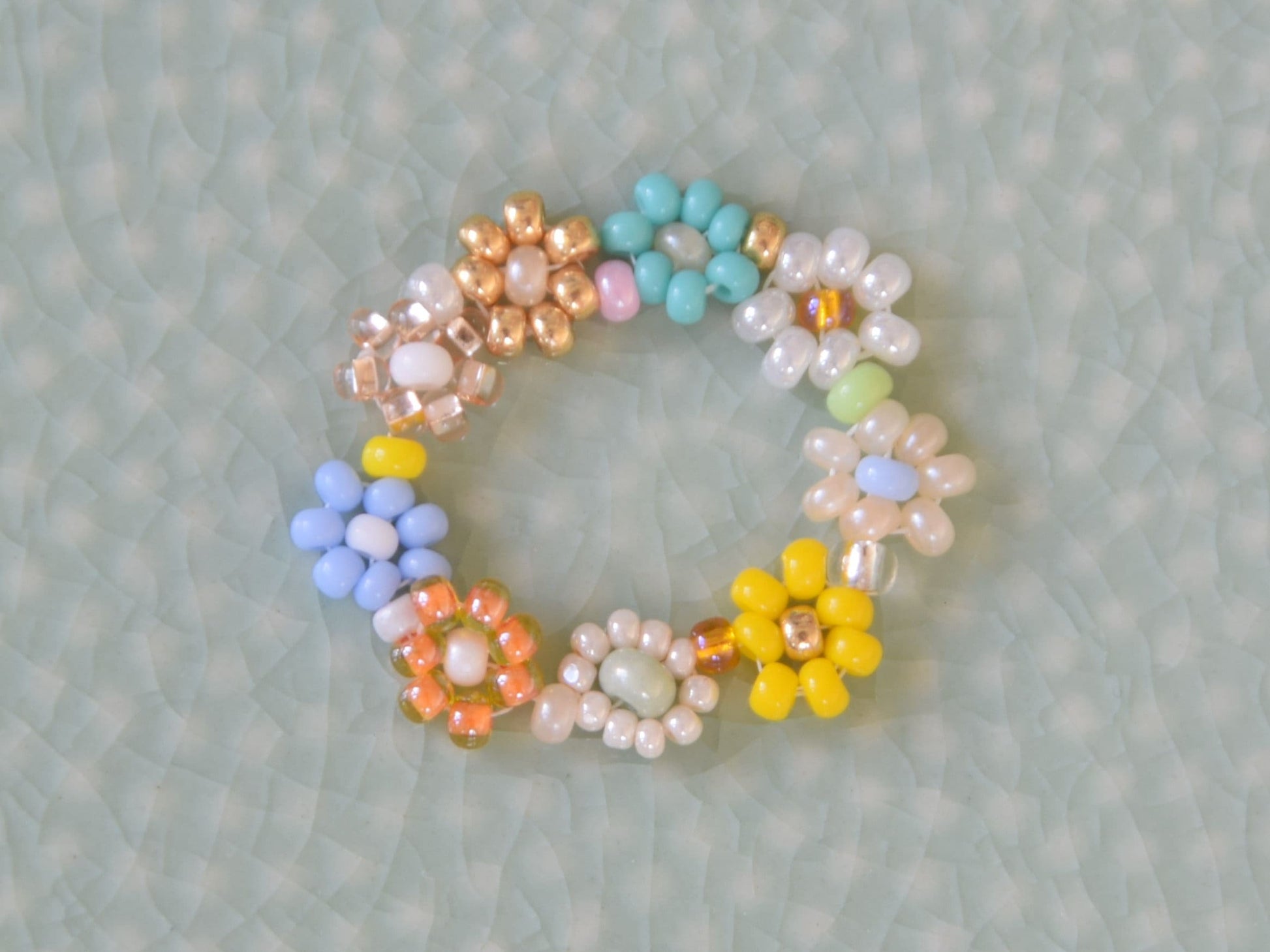 A colorful ring laying flat on a green surface. The ring consists of small round glass beads of several different colors, arranged into flowers.