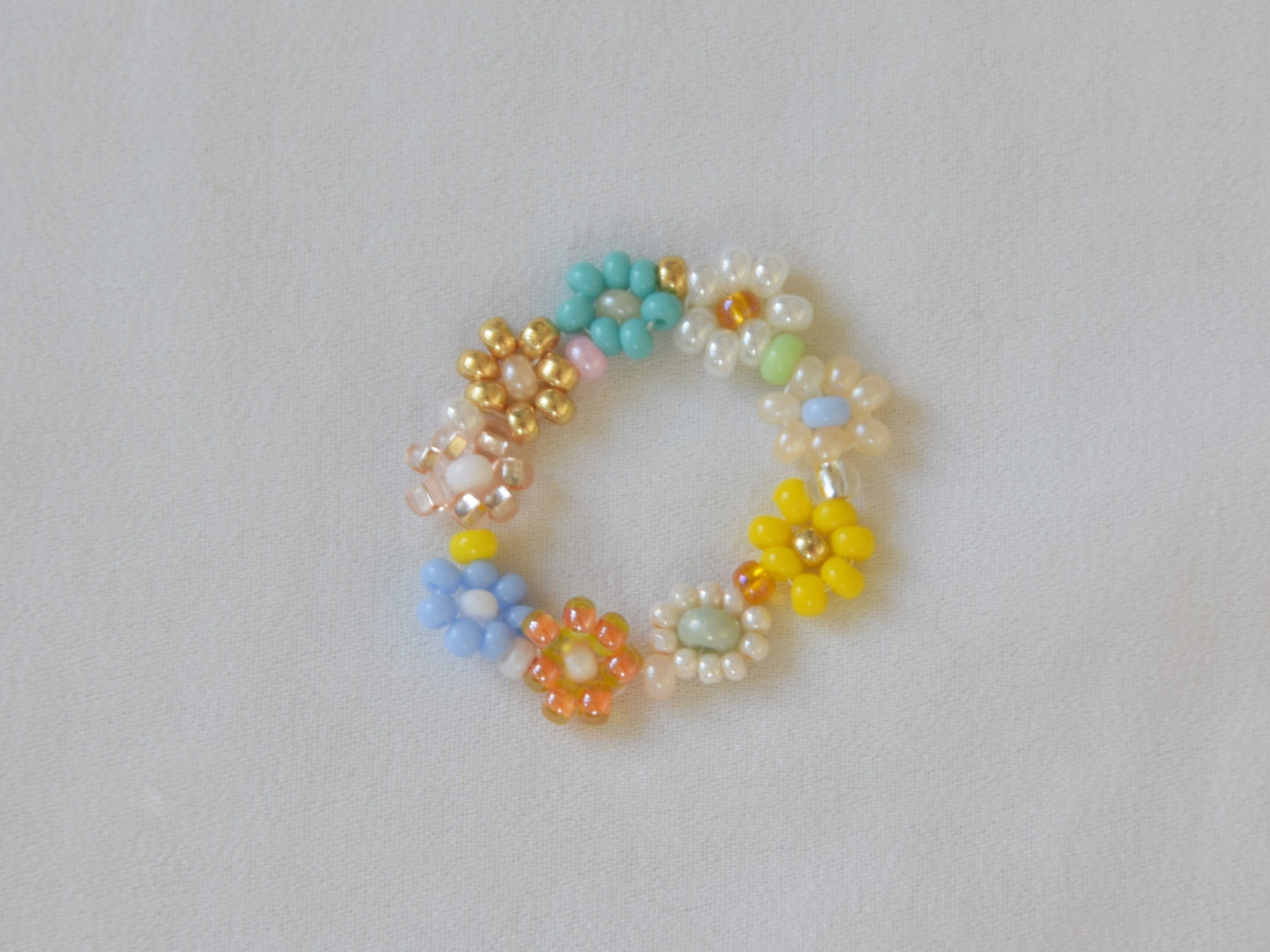 A colorful ring laying flat on a white surface. The ring consists of small round glass beads of several different colors, arranged into flowers.