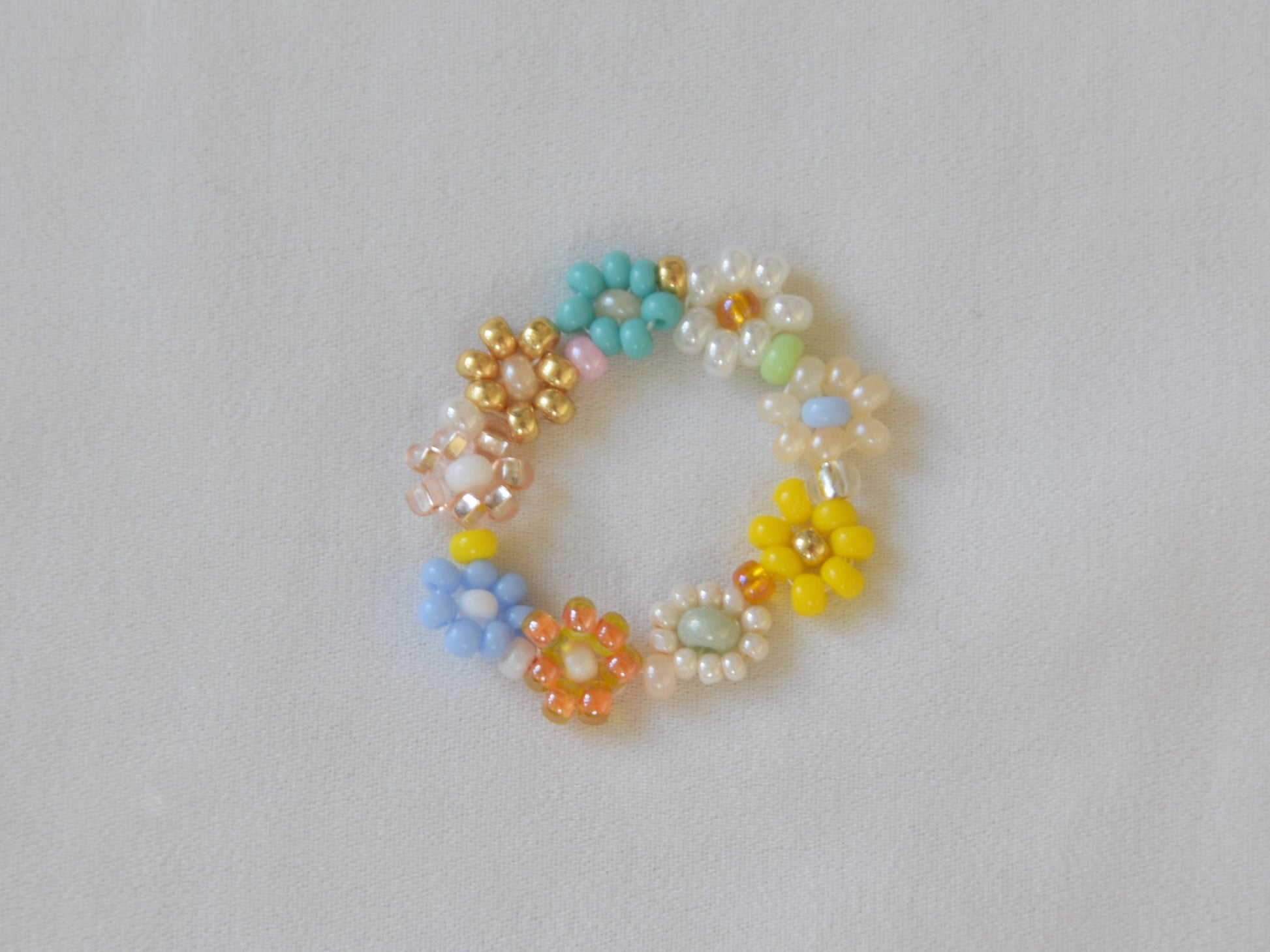 A colorful ring laying flat on a white surface. The ring consists of small round glass beads of several different colors, arranged into flowers.