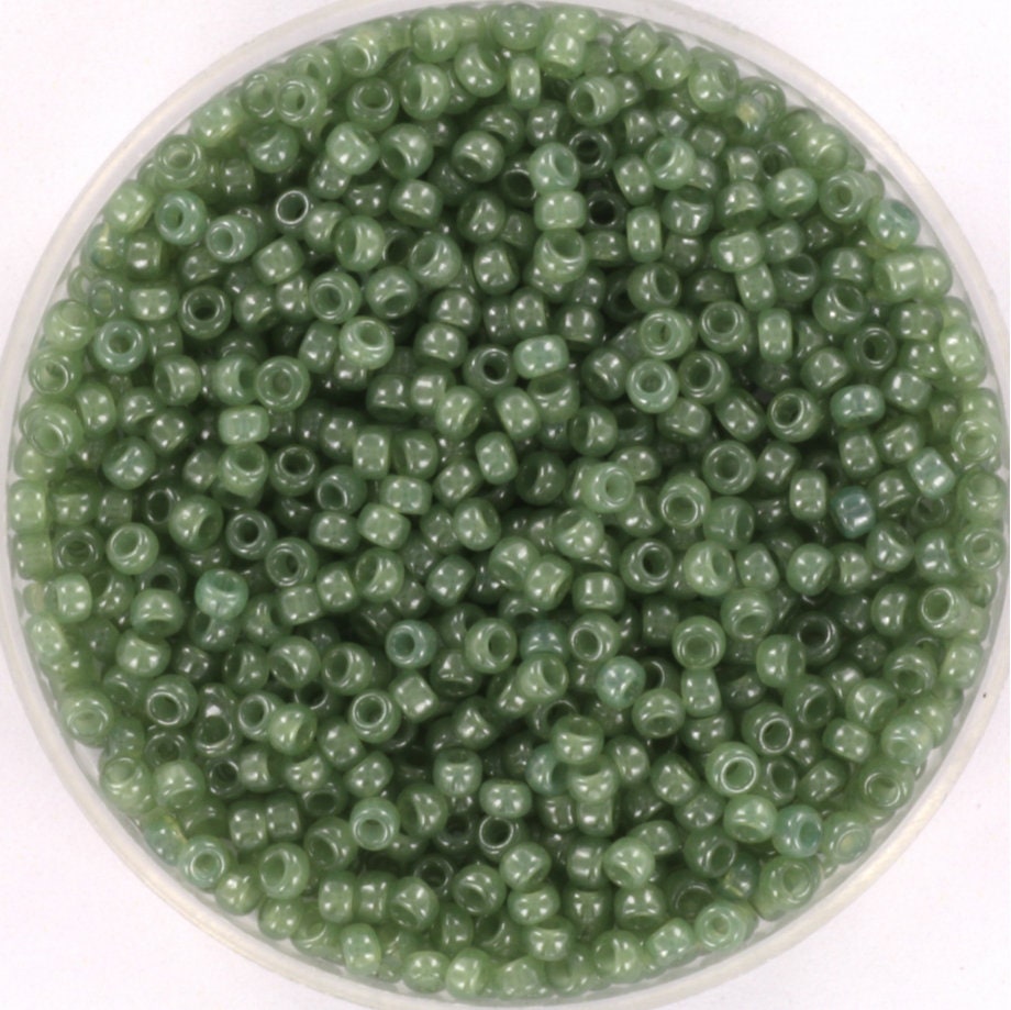 Translucent green seed beads, 2mm in size and round in shape. The image shows a round bowl full of seed beads on a white background