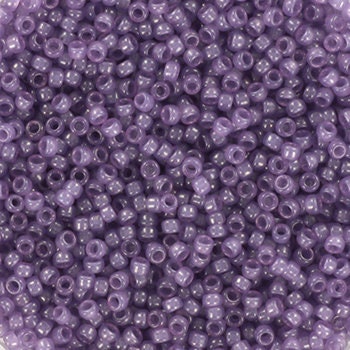 Translucent purple seed beads, 1.5mm in size and round in shape. The image is a close-up of a bowl of full of seed beads so that the beads fill the entire image.