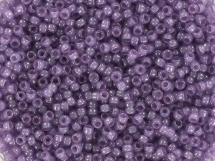 Translucent purple seed beads, 1.5mm in size and round in shape. The image is a close-up of a bowl of full of seed beads so that the beads fill the entire image