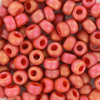 Red seed beads with rainbow luster, 4mm in size and round in shape. The image is a close-up of a bowl of full of seed beads so that the beads fill the entire image