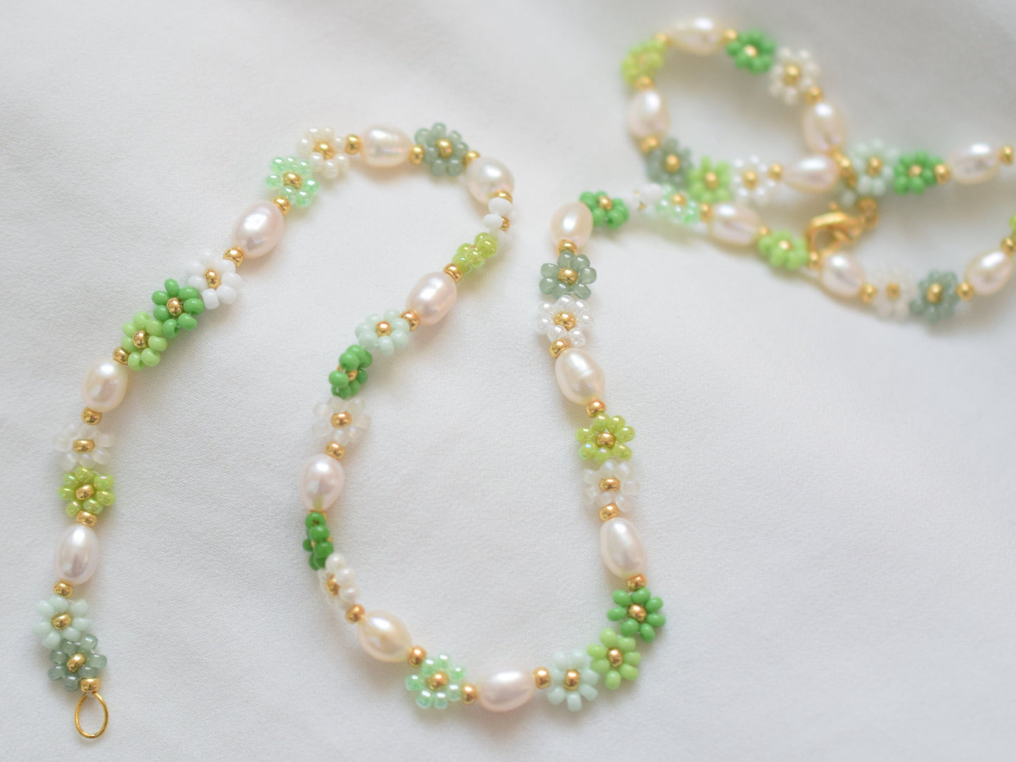 Beaded necklace with seed beads and oval freshwater pearls. The seed beads are in various shades of green and white, arranged in little flowers with a gold bead as the center of each flower. The necklace has a gold colored lobster clasp.