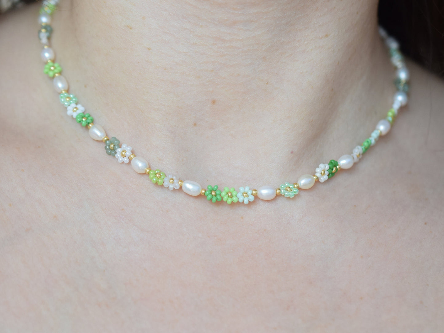 Beaded necklace with seed beads and oval freshwater pearls. The seed beads are in various shades of green and white, arranged in little flowers with a gold bead as the center of each flower. The necklace has a gold colored lobster clasp.