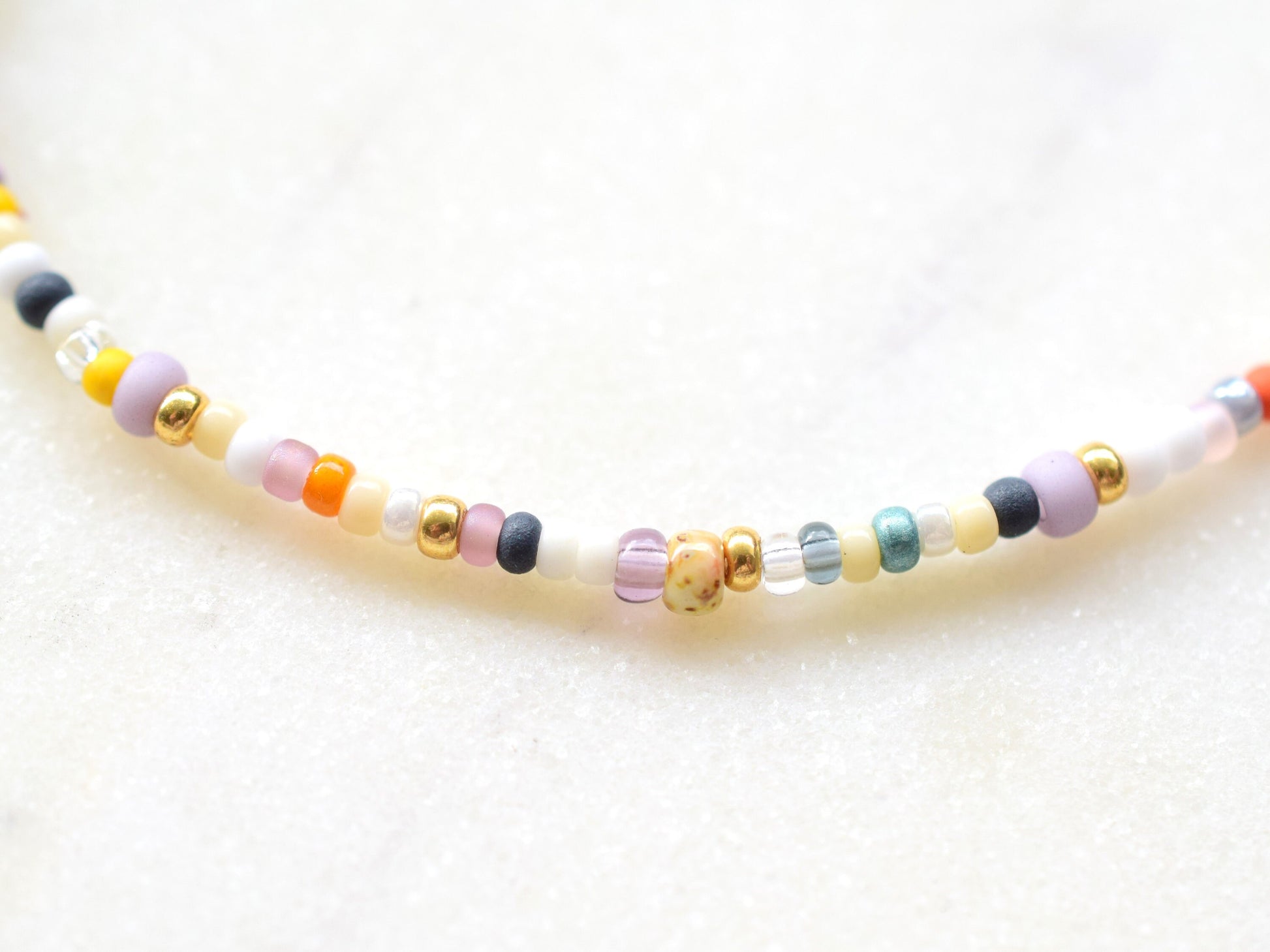 One stranded beaded necklace in a mix of seed beads in different colors and sizes. The colors are mostly whites and fall colors, like orange, purple, yellow, brown, grey.