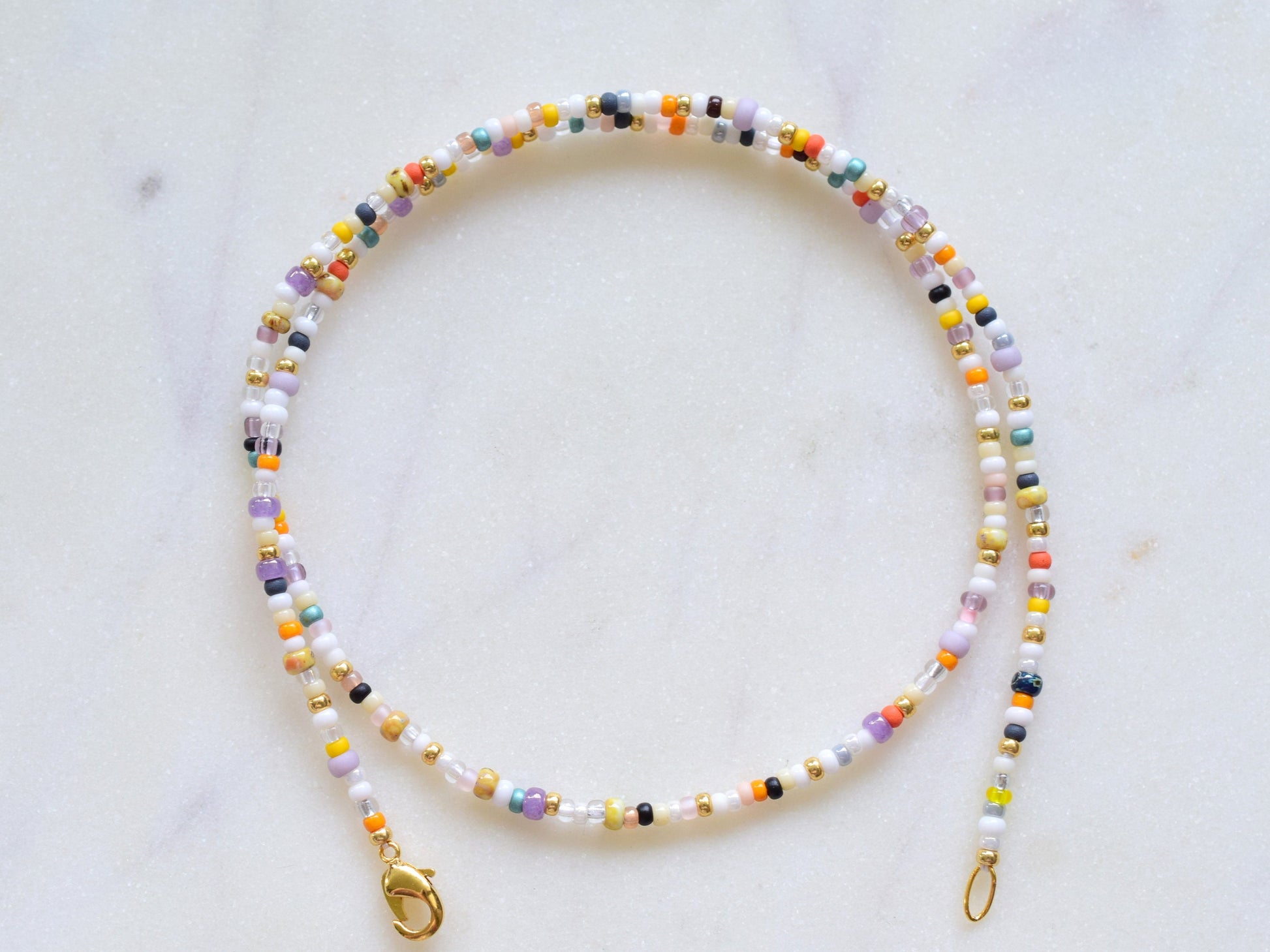 One stranded beaded necklace in a mix of seed beads in different colors and sizes. The colors are mostly whites and fall colors, like orange, purple, yellow, brown, grey.