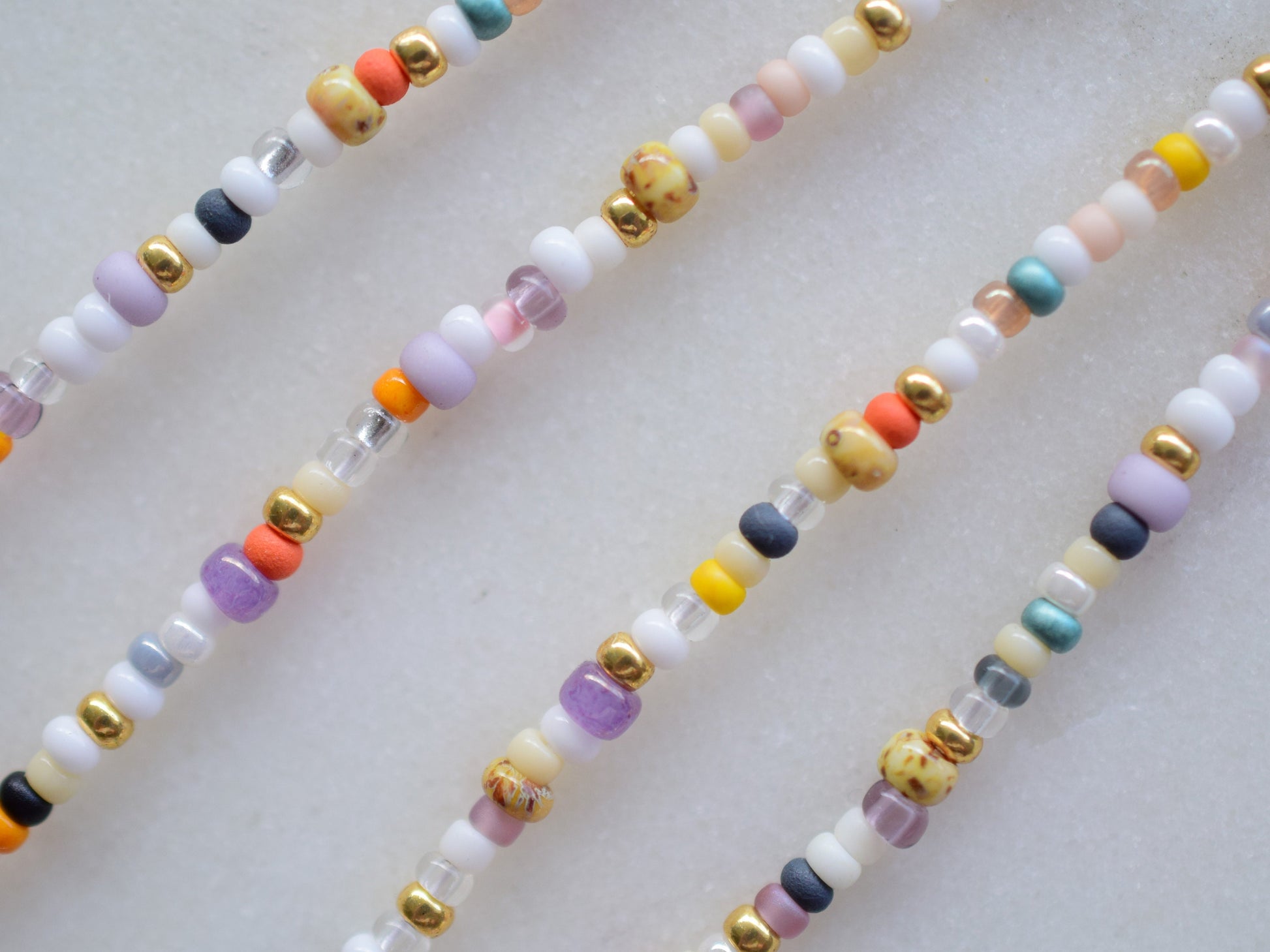 One stranded beaded necklace in a mix of seed beads in different colors and sizes. The colors are mostly whites and fall colors, like orange, purple, yellow, brown, grey.