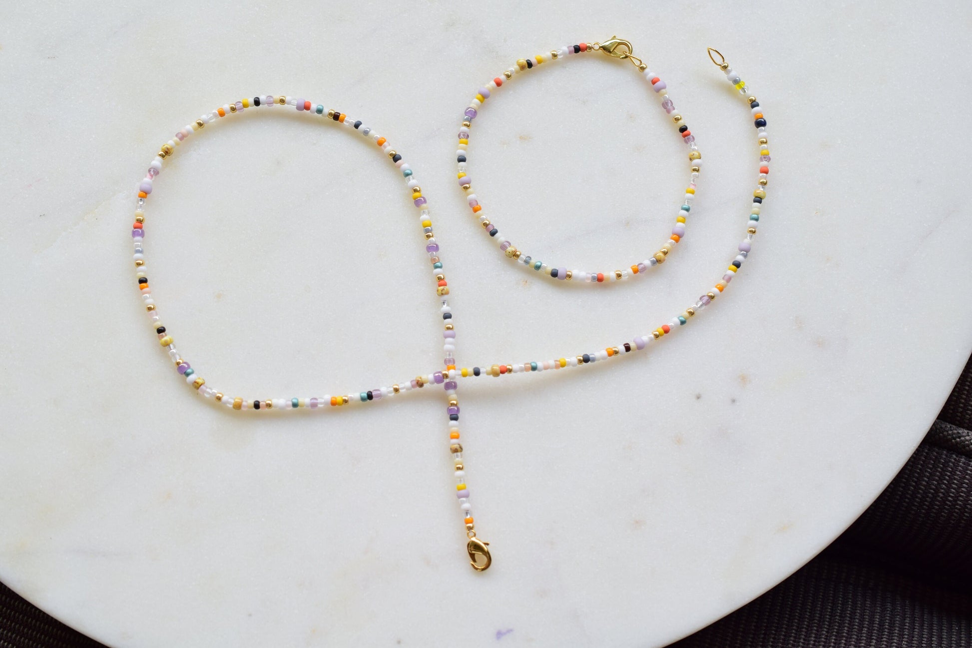 One stranded beaded necklace in a mix of seed beads in different colors and sizes. The colors are mostly whites and fall colors, like orange, purple, yellow, brown, grey.