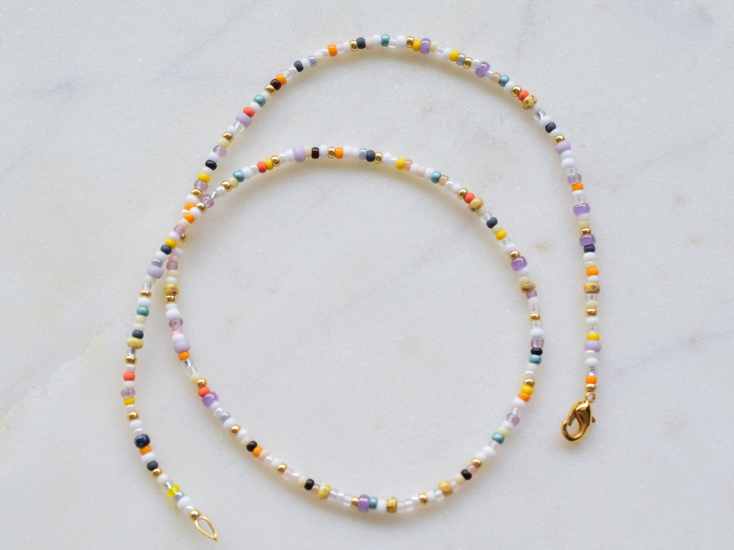 One stranded beaded necklace in a mix of seed beads in different colors and sizes. The colors are mostly whites and fall colors, like orange, purple, yellow, brown, grey.