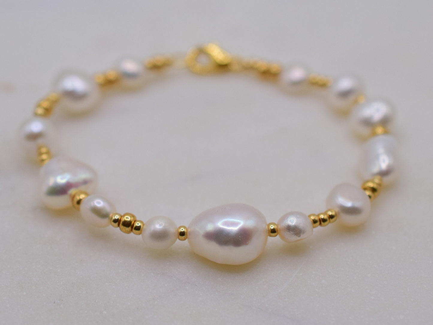 Beaded bracelet with gold seed beads and freshwater pearls in different shapes and sizes.