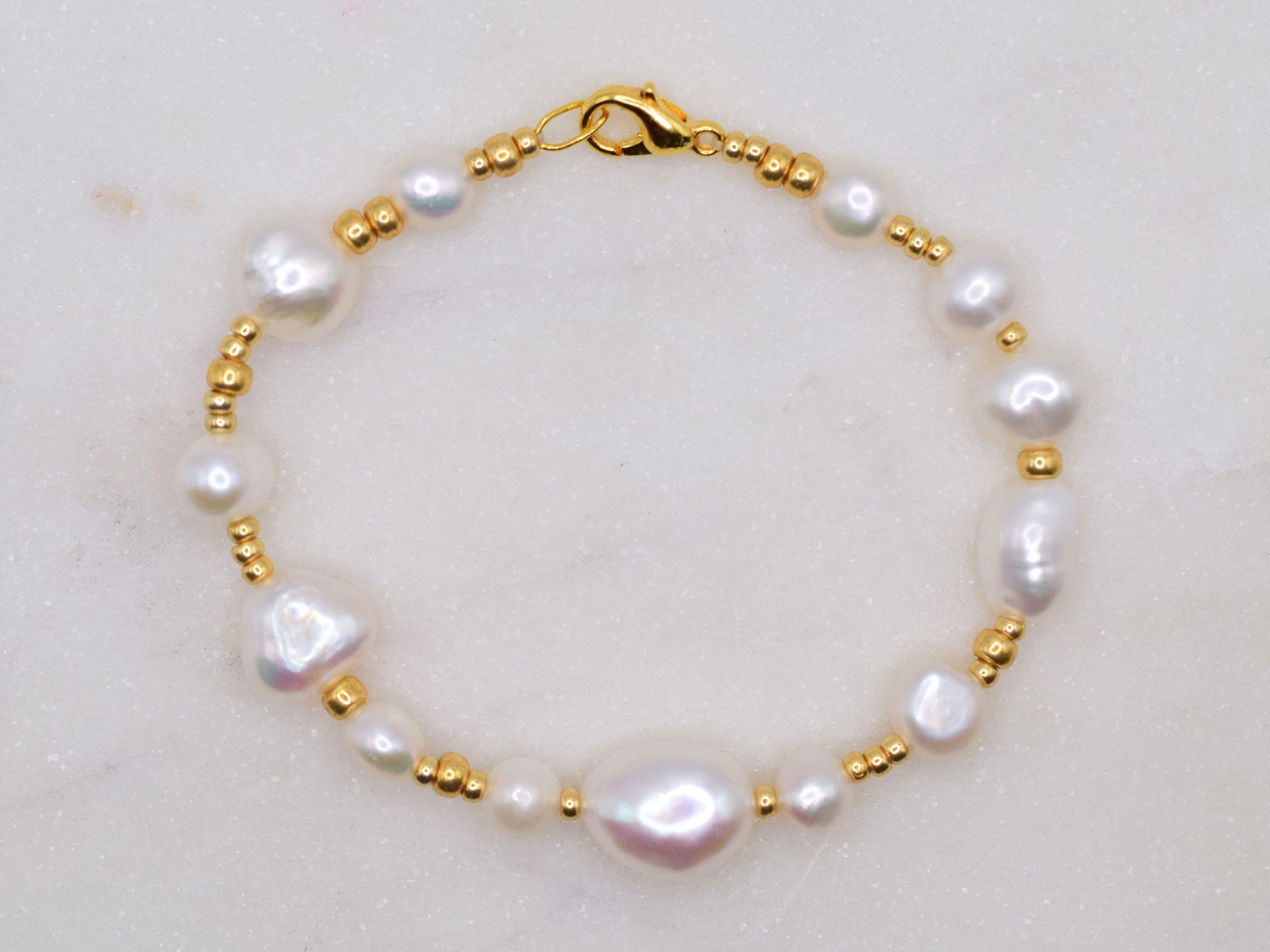 Beaded bracelet with gold seed beads and freshwater pearls in different shapes and sizes.